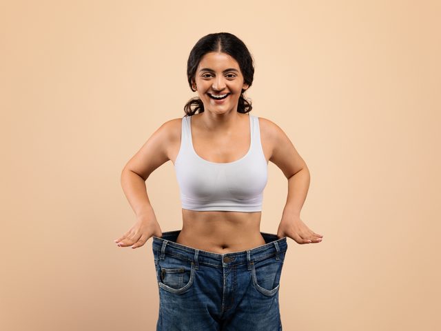 A woman holding out loose-fitting jeans after body contouring and weight loss